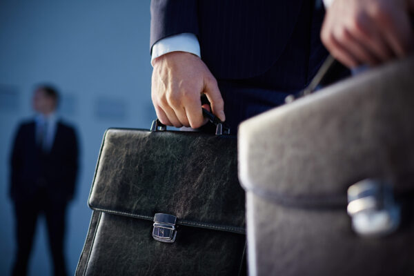 Business partners Cropped image of business partners carrying briefcases on the foreground while their colleague standing on the background